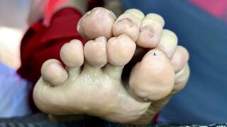 A very Tiny human being is placed on the soles of a Giantess' feet