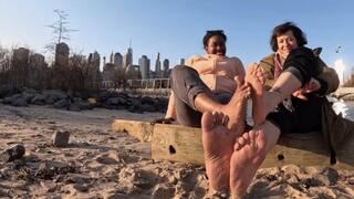 Playing footsie while chatting on beach with SluttySoles, size 9 and 11 comparison, sandy and wet feet, NYC in back