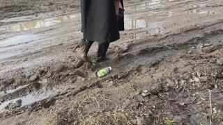 A girl in high-heeled leather boots walks through mud and then falls into it with her knees (short version)