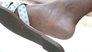 Beautyful feet soles with slippers in crossed legs, foot fetish close-up details, admiration.