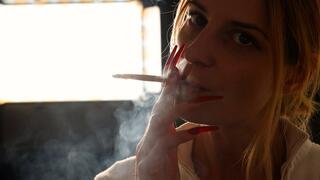 Blonde Eve with long red nails, exhaling smoke in slow motion