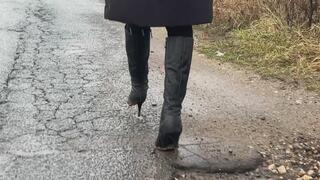 A girl in high-heeled leather boots walks through mud in bad weather, slips on mud and gets her boots dirty