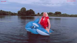 Alla rides an inflatable squeaky whale on a lake in the evening
