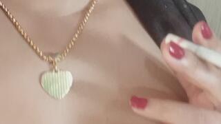 A beautiful brunette smokes a cigarette with her lovely breasts on display.