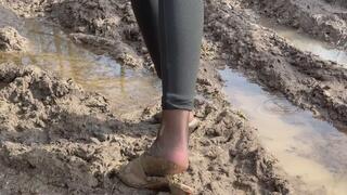 A girl walks through the woods in high-heeled sandals and steps on mud, loses her shoes, slips