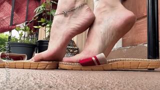 Slippers dangle, arches, and soles show, below my chair pov, long sexy red dress, white toes