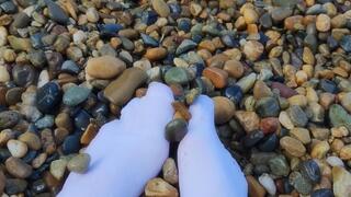 Playing with my feet in white socks with pebbles on the beach