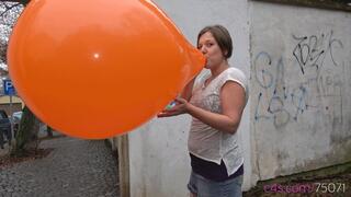 Simona inflates a giant orange balloon outside (4K quality)