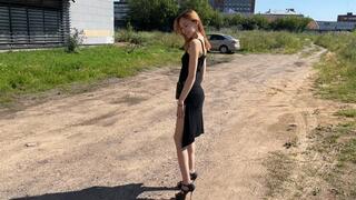 A girl in high-heeled shoes walks along a broken road where there is dust and dirt and rejoices at how her shoes and feet become dirty