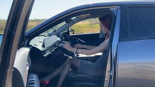 A girl in high-heeled shoes is stuck alone in a field with an idle car, she tries to move it from its place but nothing comes out