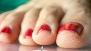 A tiny guy admires the legs of a giantess while the red varnish dries on her toenails