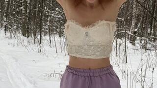 A girl in a terrible frost stands in the forest in ballet flats, shorts and a top and shakes from the cold