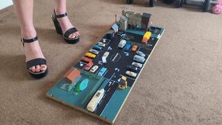 Giantess Raven Lee crushes a model set with lots of small cars & buildings in big black wedges with painted toenails high right view