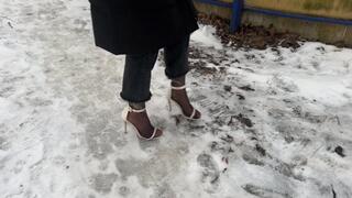 A girl in high-heeled shoes with open toes went out for a walk in winter, her heels are sliding on the ice and she is always slipping